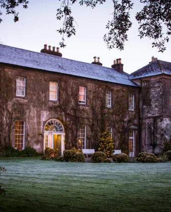 Georgian manor hotel at dusk with lit entrance, festive fairy-lit hedges, frosted lawn and mature trees — peaceful countryside stay