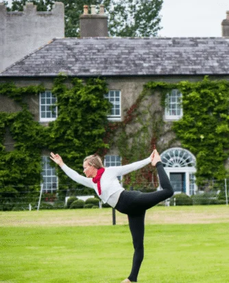 Guest practising yoga on lush lawn in front of ivy-covered historic hotel with elegant windows, offering serene retreat experience.