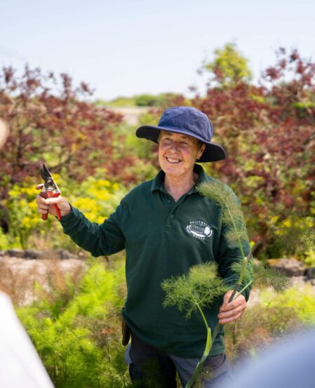 Friendly gardener hosting a garden tour amidst lush greenery at a countryside hotel.