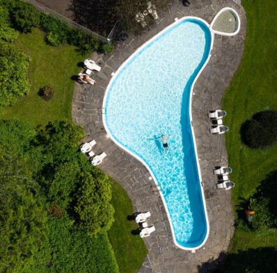 Aerial view of outdoor pool surrounded by lush greenery, with sun loungers and guests relaxing, ideal for tranquil retreats.