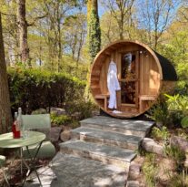 Cosy wooden sauna nestled in tranquil forest setting with robes, garden seating, and refreshments for a relaxing escape.