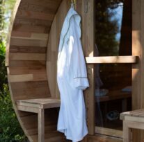 Luxury wooden sauna exterior with hanging plush robe and slippers, surrounded by greenery at tranquil hotel spa retreat.