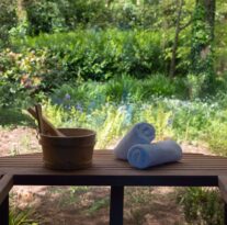 Cosy hotel veranda with garden view, featuring rolled towels and a wooden bucket, perfect for relaxation and nature enjoyment.
