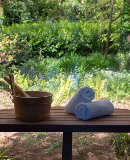 Cosy hotel veranda with garden view, featuring rolled towels and a wooden bucket, perfect for relaxation and nature enjoyment.