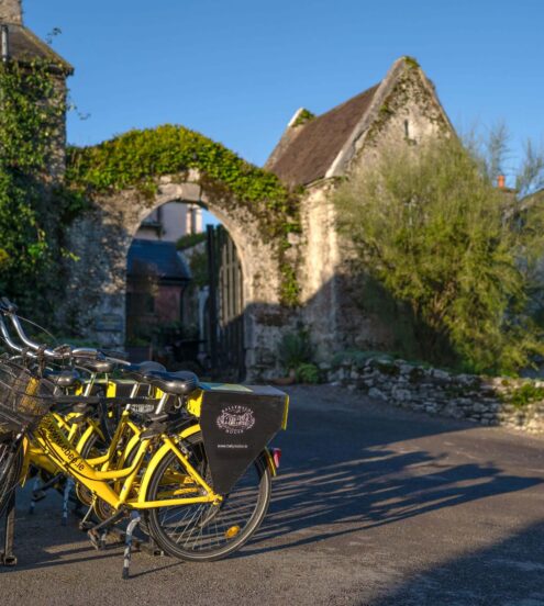Charming hotel entrance with vintage stone archway, lush greenery, and rental bicycles for guest exploration.