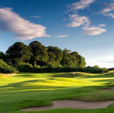 Lush green golf course surrounded by trees under a blue sky, offering a serene and picturesque outdoor experience.