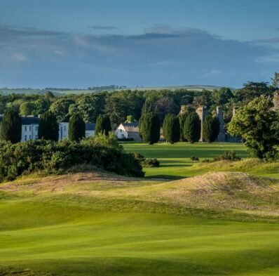 Lush green golf course with serene countryside views, historic hotel in the background, perfect for a relaxing getaway.
