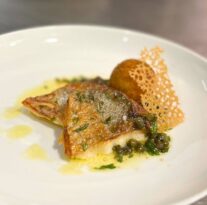 Elegant gourmet fish dish with crispy skin, capers, herb sauce, and decorative garnish on a pristine white plate.