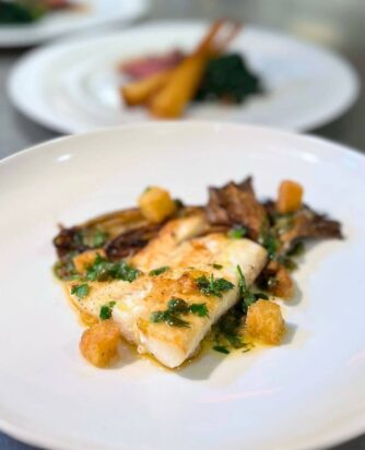 Gourmet fish dish with herbs, accompanied by roasted vegetables, reflecting luxury dining at our hotel restaurant.