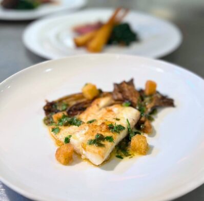 Gourmet fish dish with herbs, accompanied by roasted vegetables, reflecting luxury dining at our hotel restaurant.