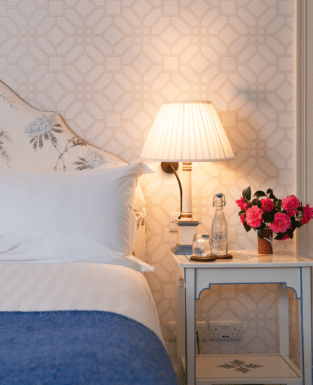 Elegant hotel room with cosy bed, floral decor, nightstand, and ambient lamp lighting. Perfect for a relaxing stay.
