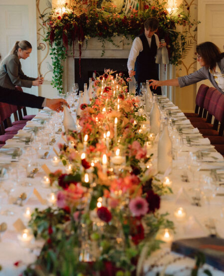 Elegant dining room setup with floral centrepieces, candlelight, and staff preparing for guests at a luxury hotel.