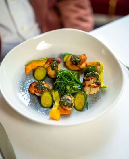 Elegant plated scallops with courgettes, flowers, and fresh herbs in a gourmet hotel restaurant setting.