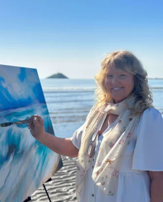 Guest painting a vibrant seascape on a sunny beach with ocean view.