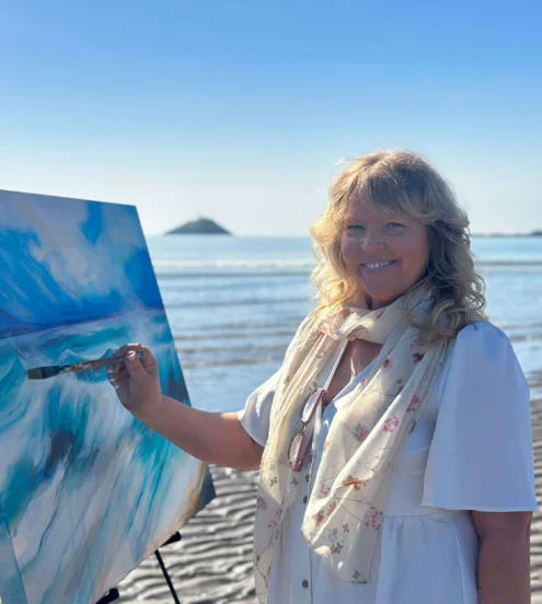 Guest painting a vibrant seascape on a sunny beach with ocean view.